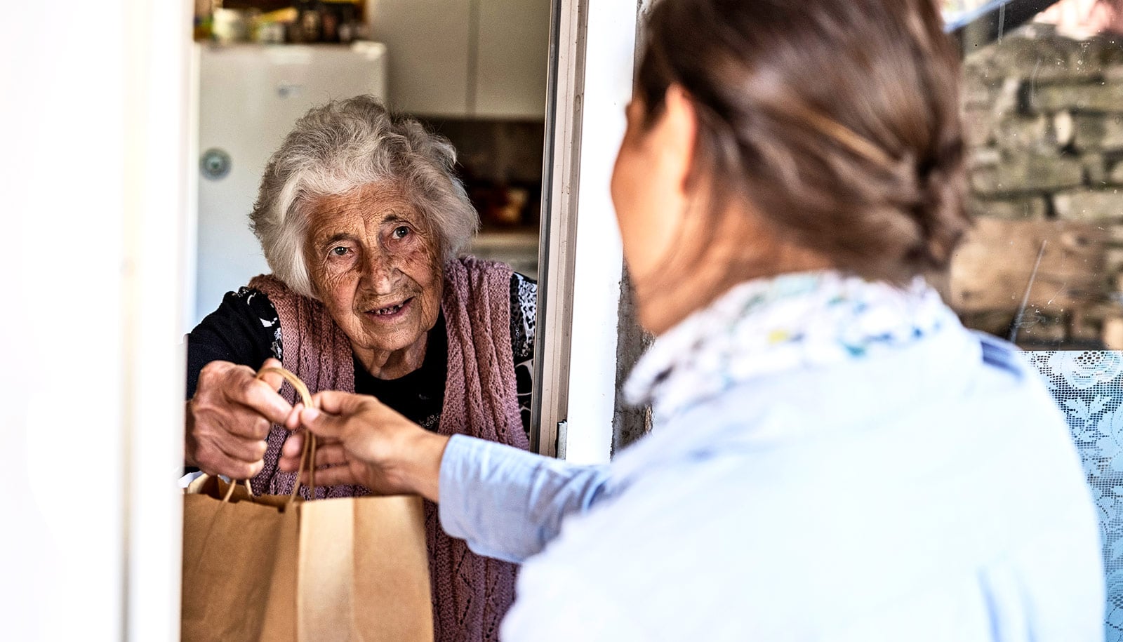 A volunteer placing a home-cooked meal on the table of a smiling elderly woman, representing community giving